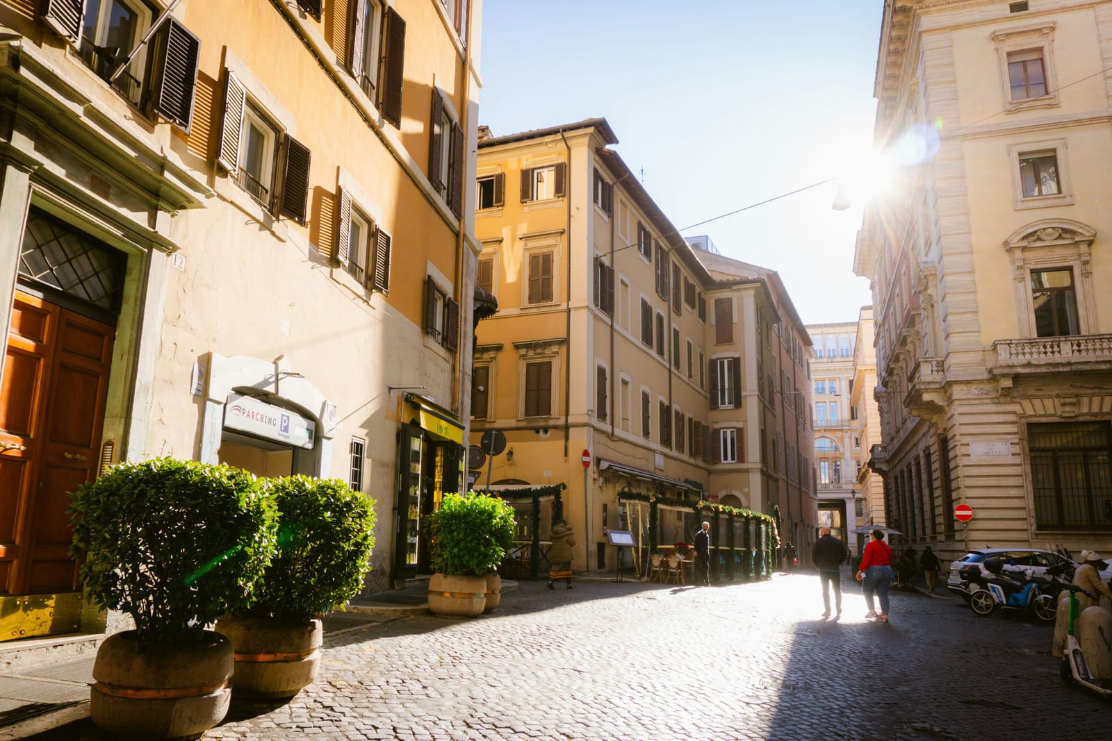 A quiet, sunny cobblestone street in central Rome with warm ochre buildings and few people, in the low season.