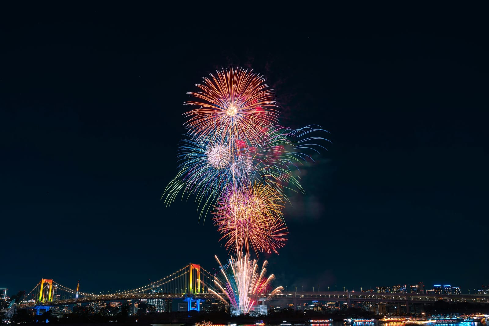 Summer fireworks over Tokyo's Rainbow Bridge at night.