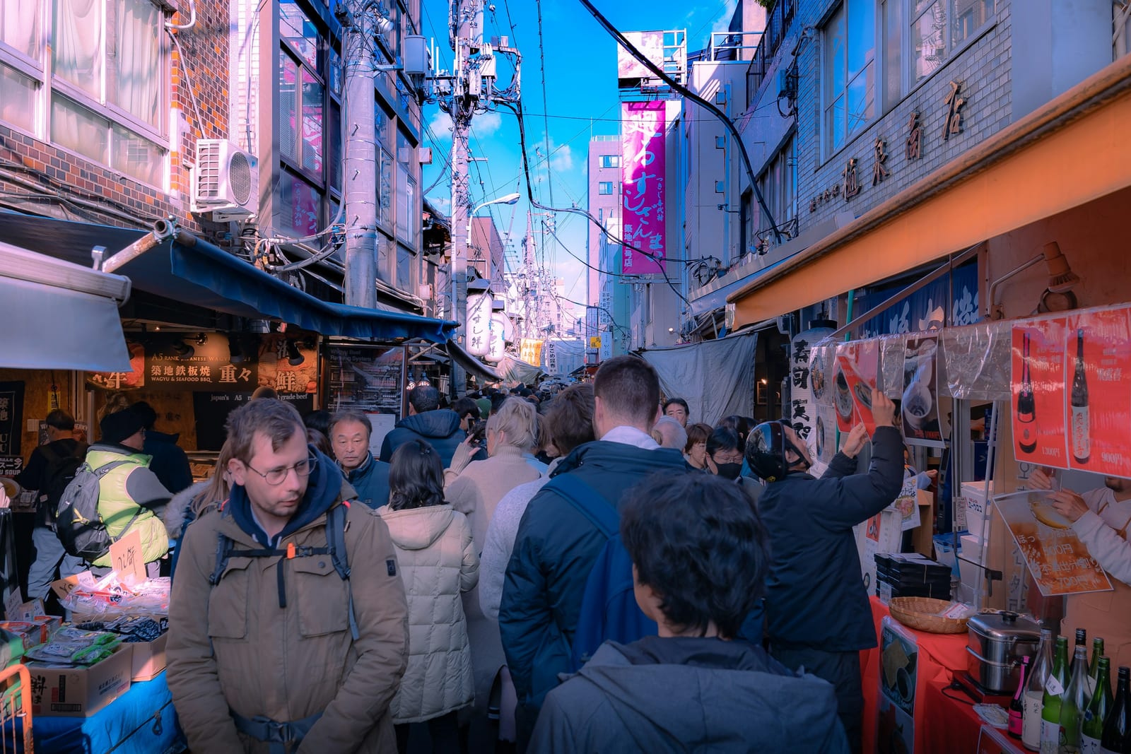 A crowd moving down a narrow Tokyo market alley packed with stalls and overhead signs.