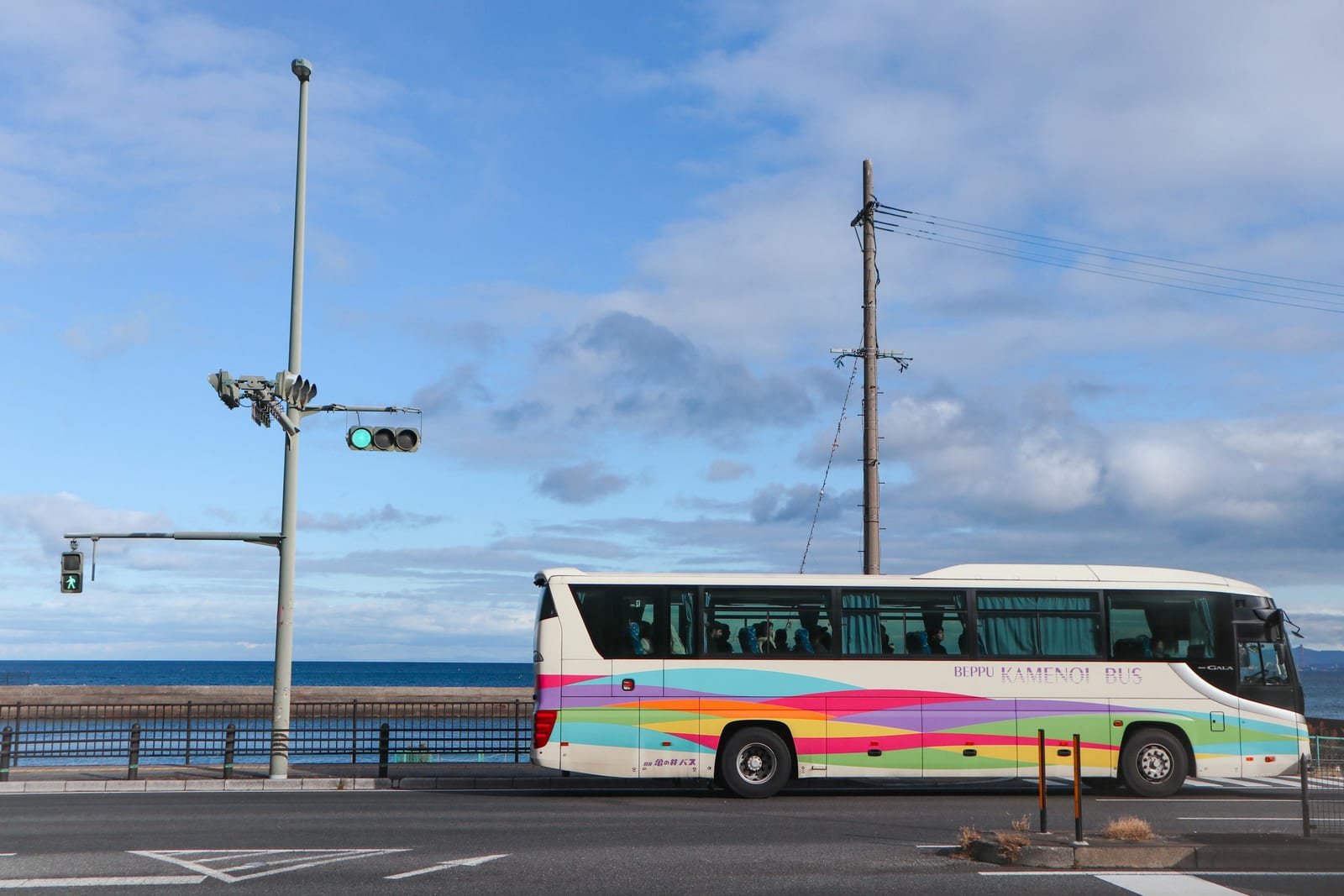 A Vineyard Transit bus travels beside a harbor road with blue water, railings, and a partly cloudy sky.