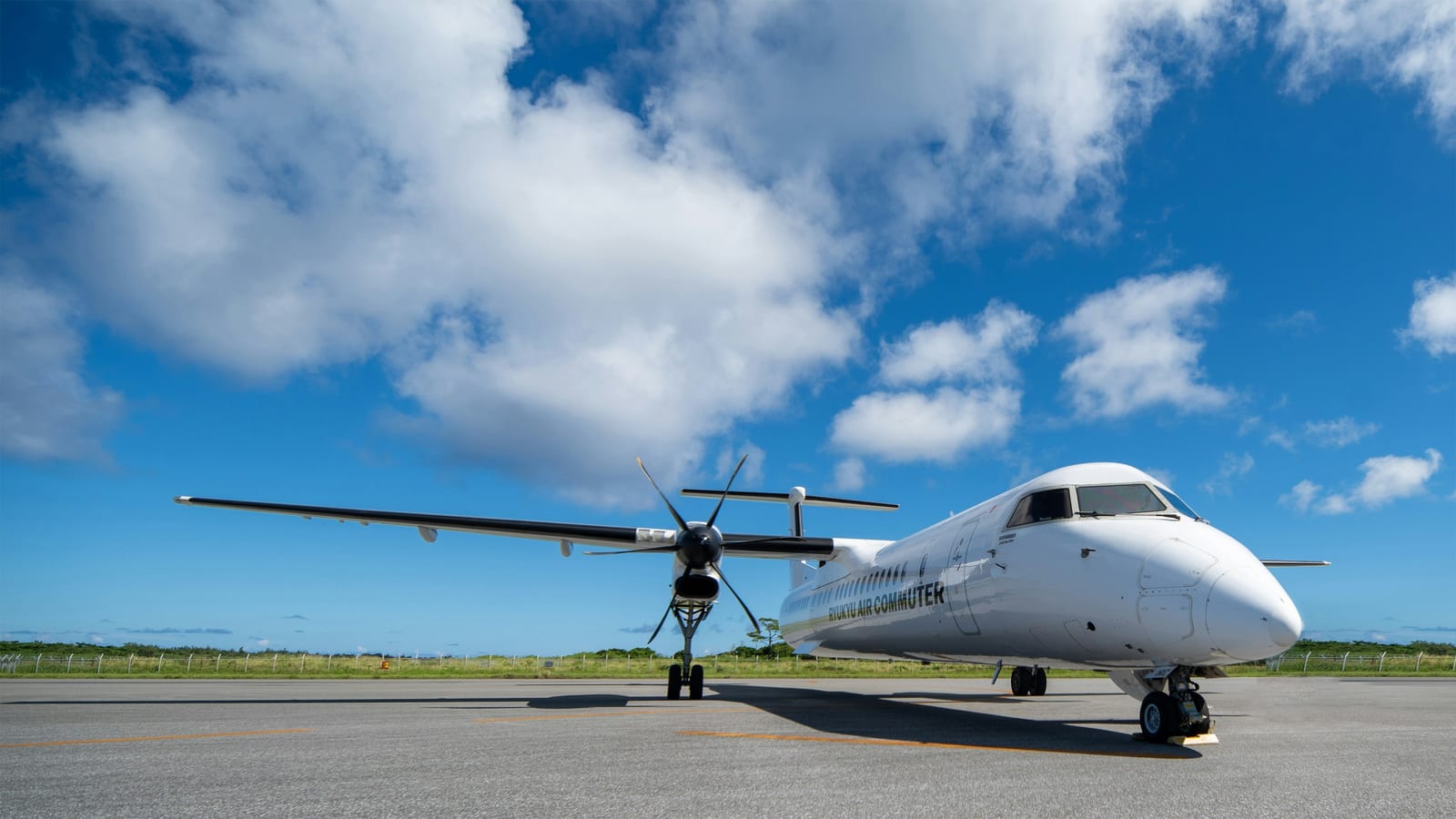 A passenger plane sits on an airport apron beneath a bright blue tropical sky.