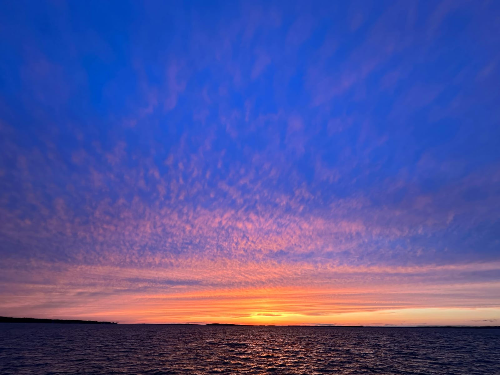 A bright sunset glows over the bay beneath pink and blue clouds.