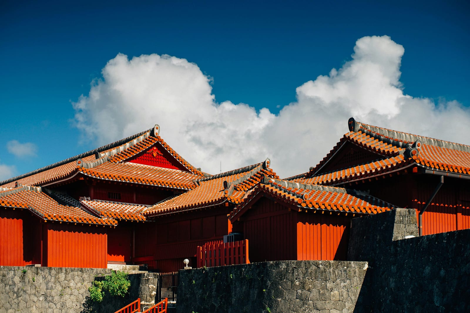 Red-tiled traditional buildings and stone walls stand beneath a bright blue sky.