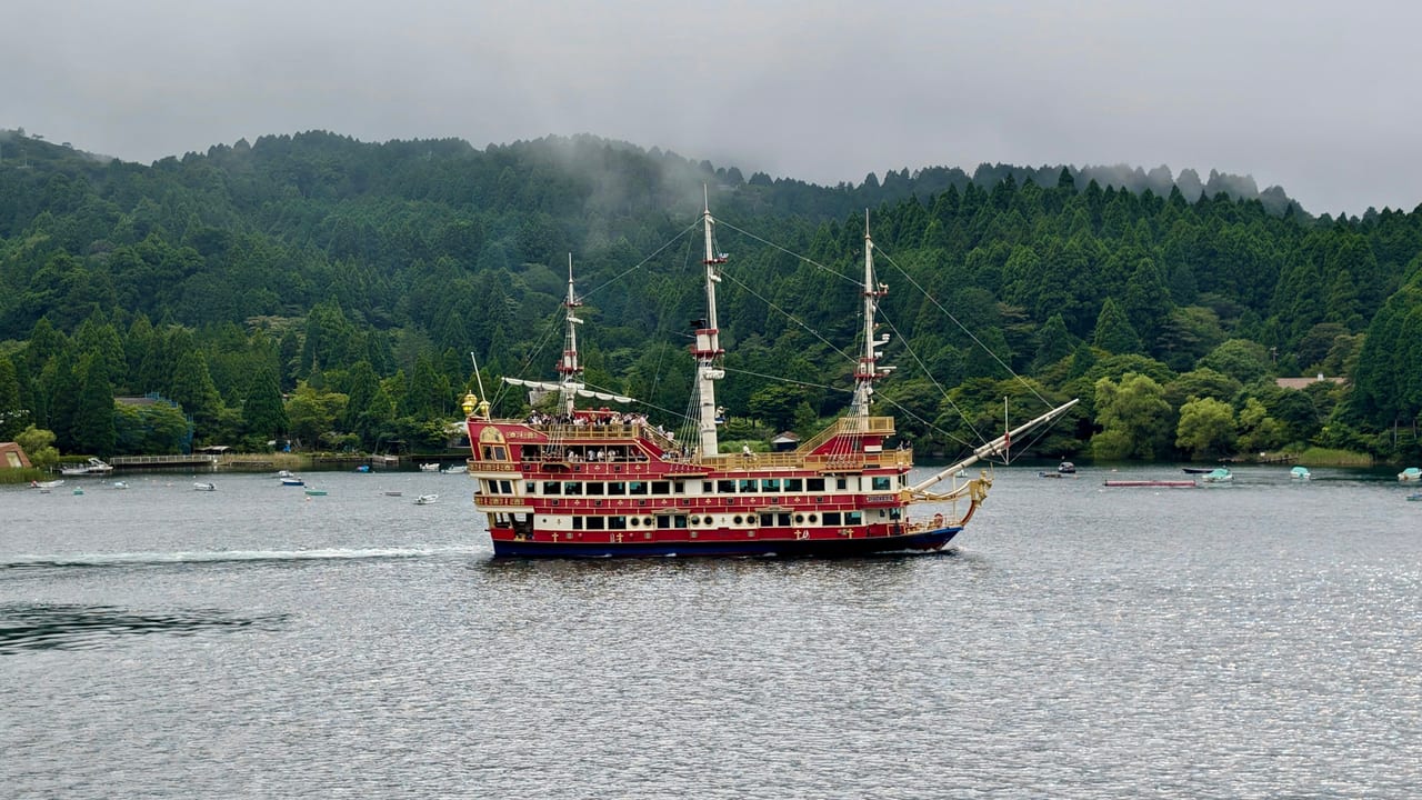 A red sightseeing galleon crosses Lake Ashi with snow-capped Mt. Fuji and a vermilion lake torii behind it.