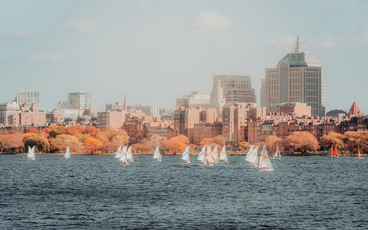 Sailboats rest on the Charles River with the Boston skyline and Prudential Tower in the background at dusk.