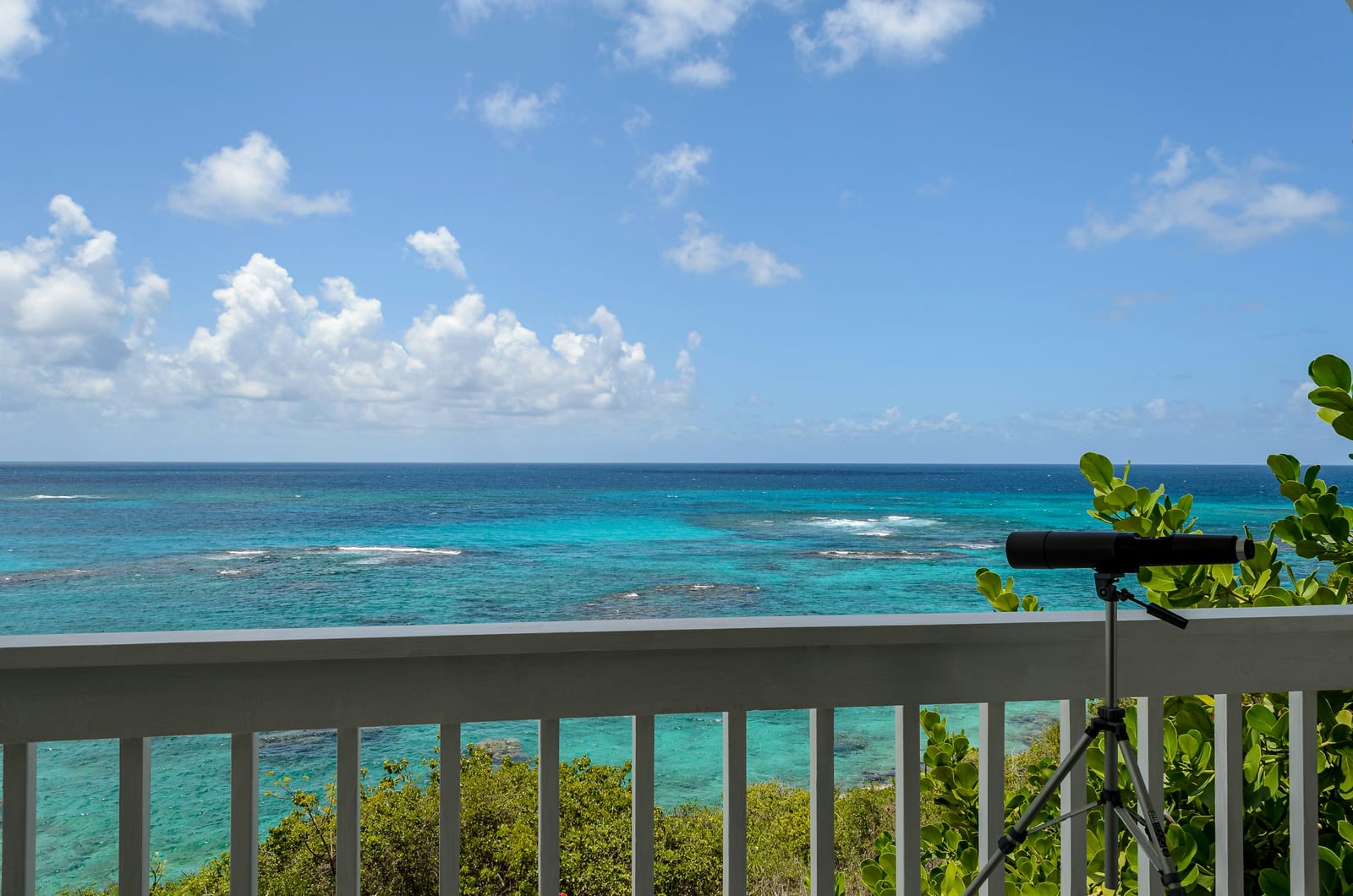 A sunny balcony overlooks clear turquoise ocean water beneath a blue sky.