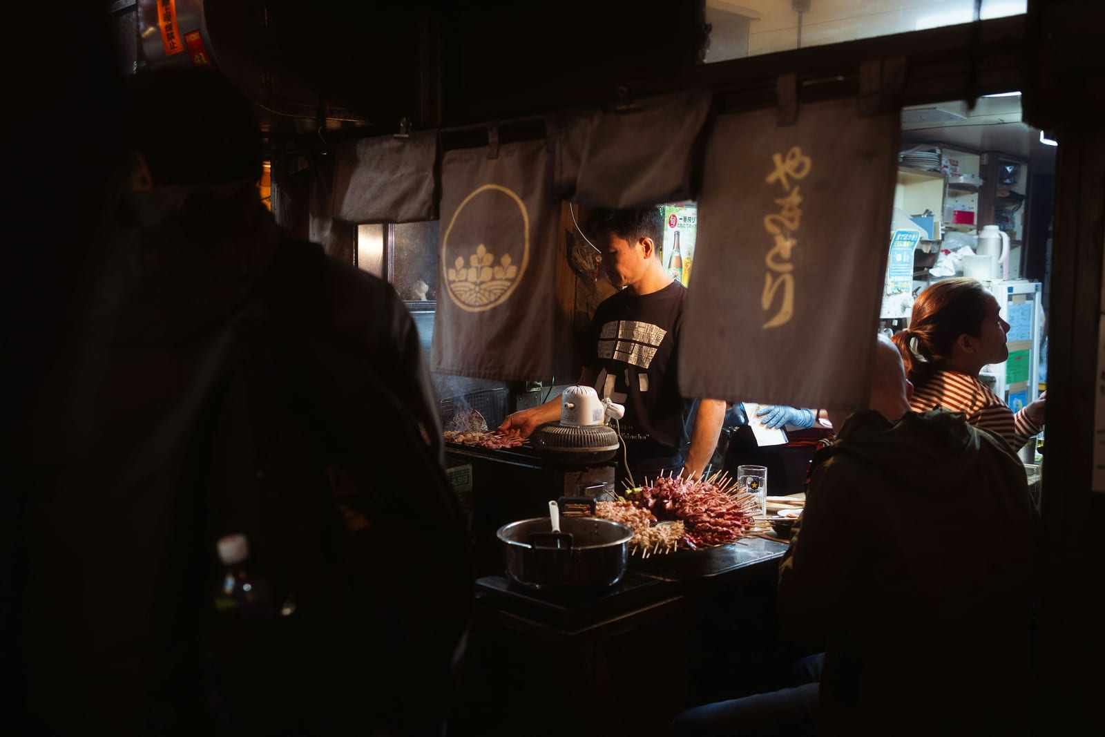 Diners packed shoulder to shoulder at a yakitori counter in Omoide Yokocho.