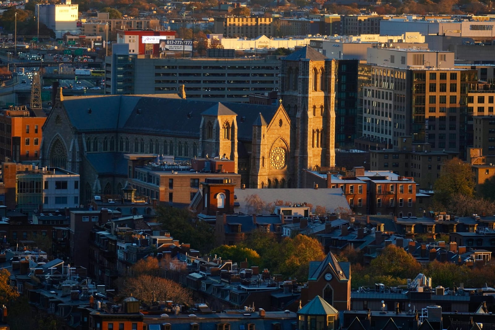 Golden-hour aerial view of Boston's South End, the Cathedral of the Holy Cross rising above Victorian rooftops.