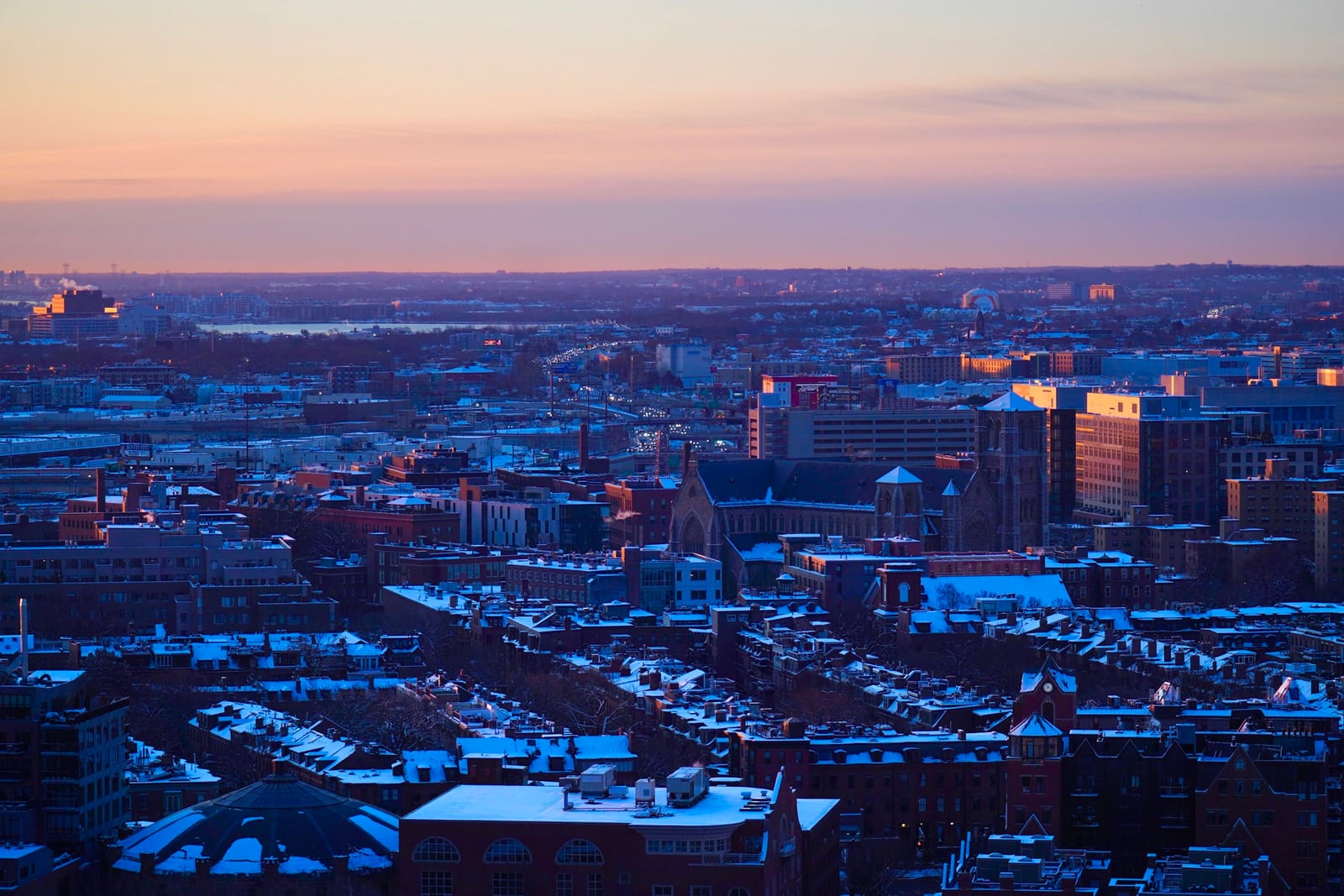 Golden-hour aerial view of Boston's South End, the Cathedral of the Holy Cross rising above Victorian rooftops