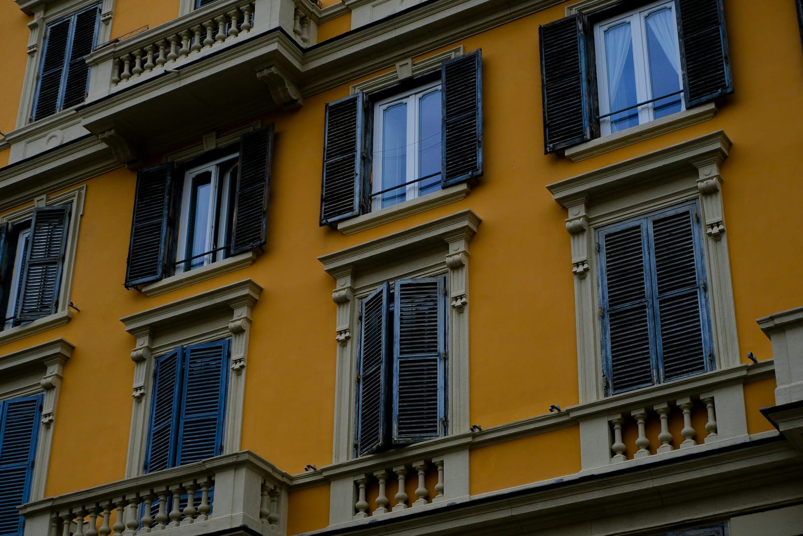 A warm ochre facade with green shutters on a quiet street in the Monti rione, Rome.