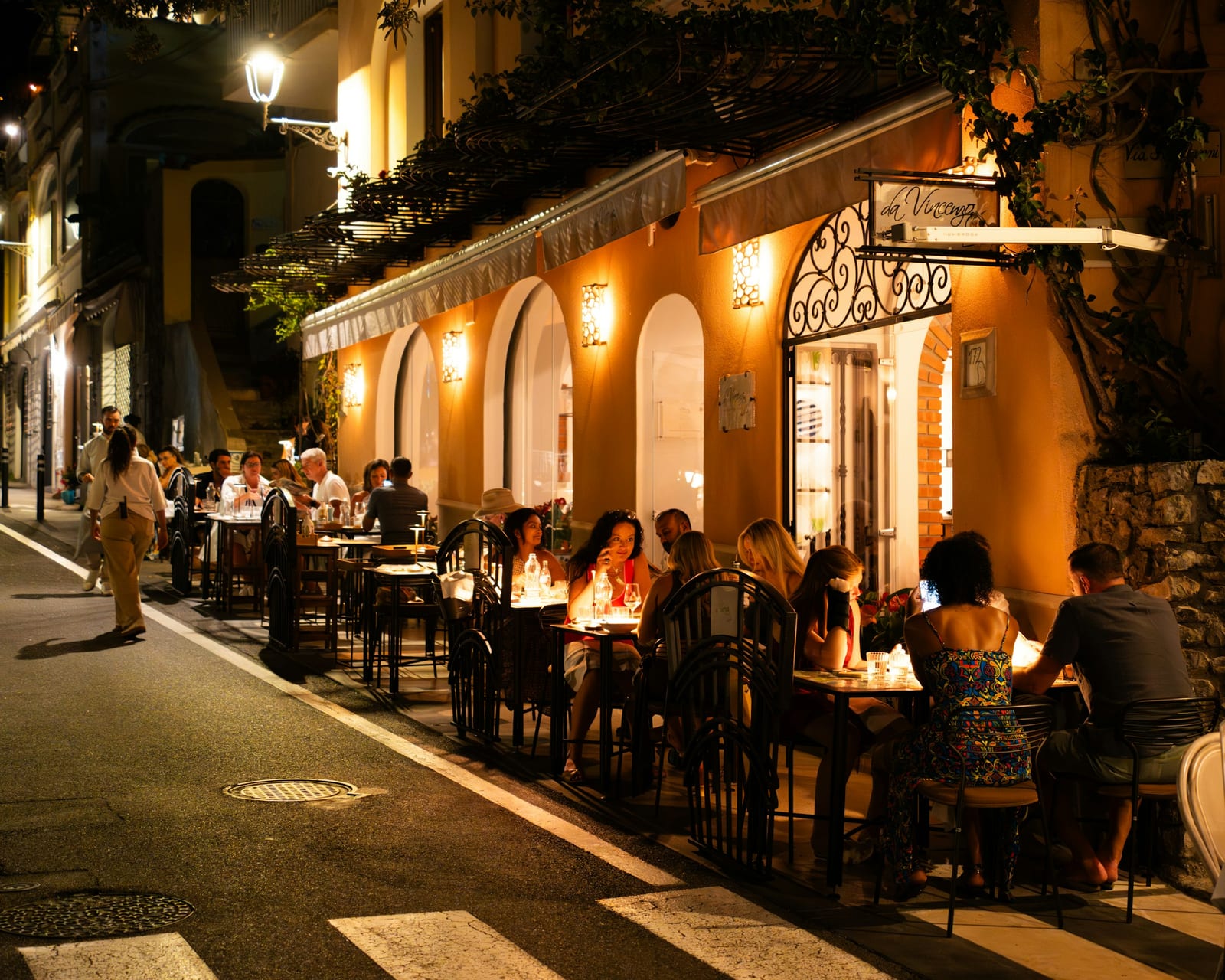 An inviting Italian restaurant street with outdoor dining and string lights.