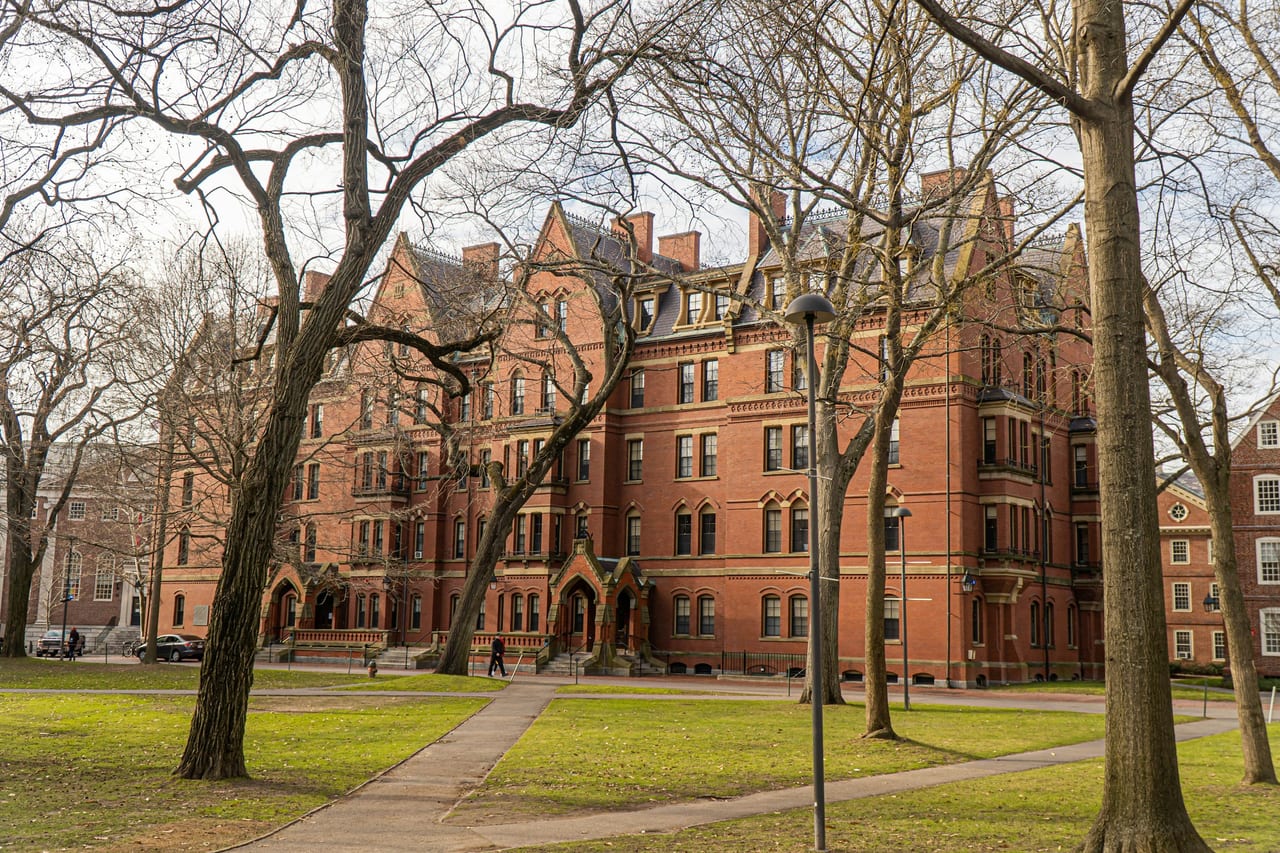 Students and visitors cross the green lawns of Harvard Yard between the red-brick dormitories.