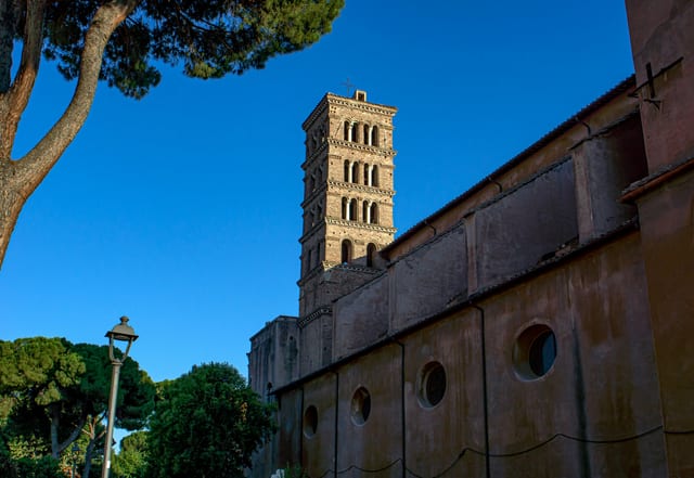 A medieval bell tower rising beside a stone church on the Aventine Hill.
