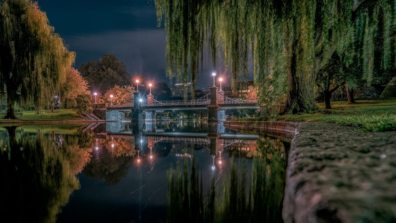 The lagoon in Boston's Public Garden reflects autumn trees and the suspension bridge on a calm morning.