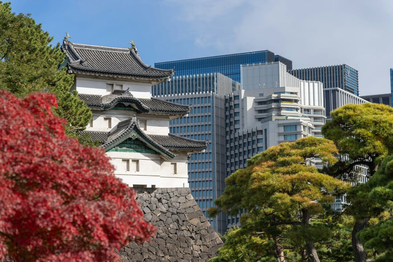 Autumn maples and clipped pines ring the still Ninomaru pond in the Imperial Palace East Gardens under a clear blue sky.