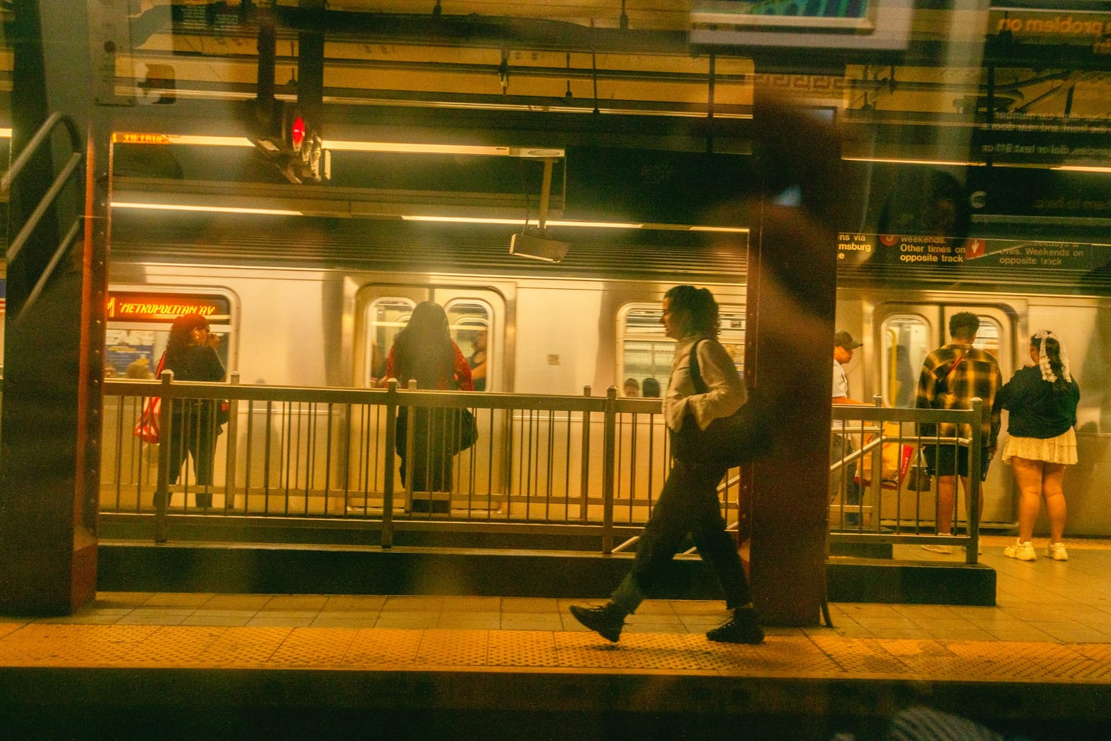A commuter walks along a brightly lit subway platform beside a stopped train.