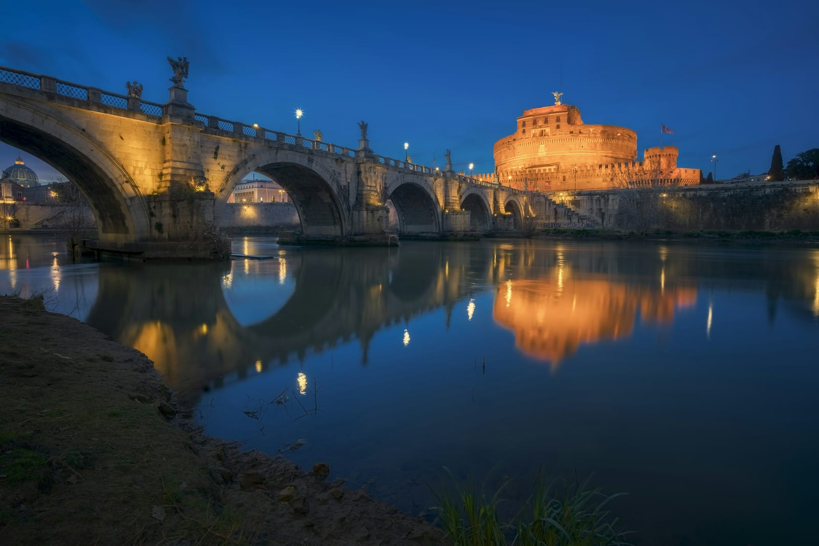Castel Sant'Angelo and its bridge reflected in the Tiber at blue hour on a summer evening.
