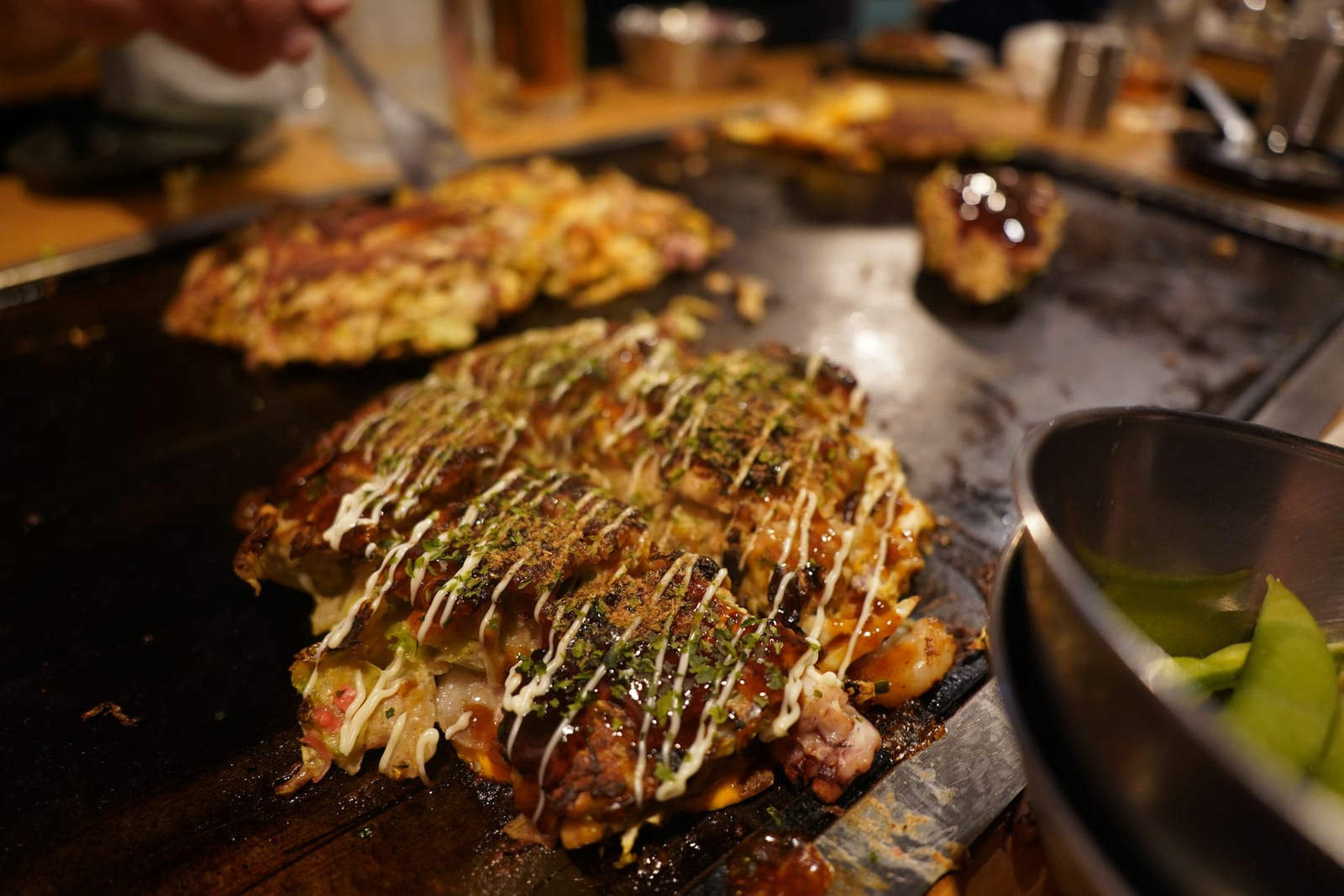 Okonomiyaki cooking on a flat teppan griddle, the firmer cousin of monjayaki.