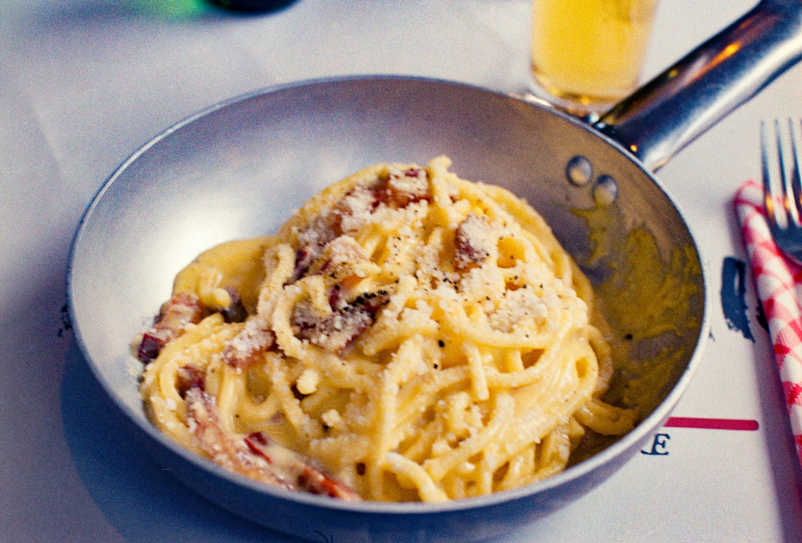 A pan of spaghetti carbonara topped with pecorino and black pepper on a paper-covered trattoria table in Rome.