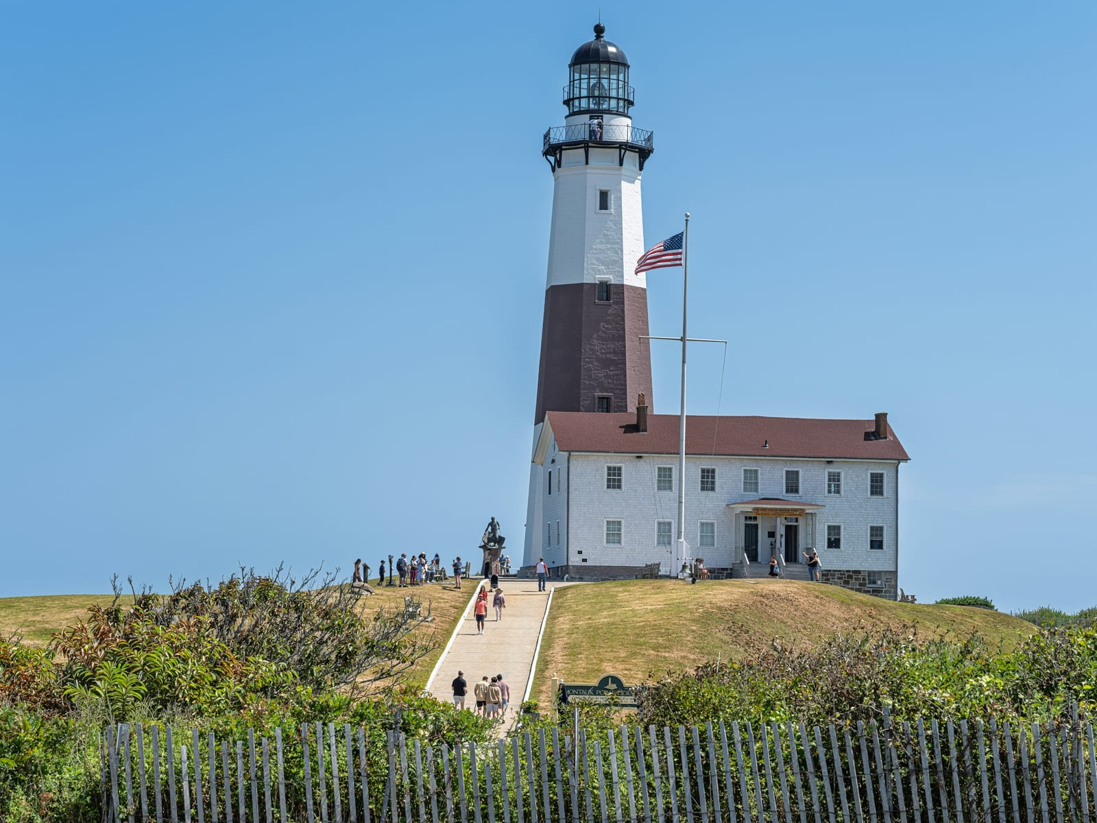 Montauk Point Lighthouse stands on a grassy dune under a clear blue sky.