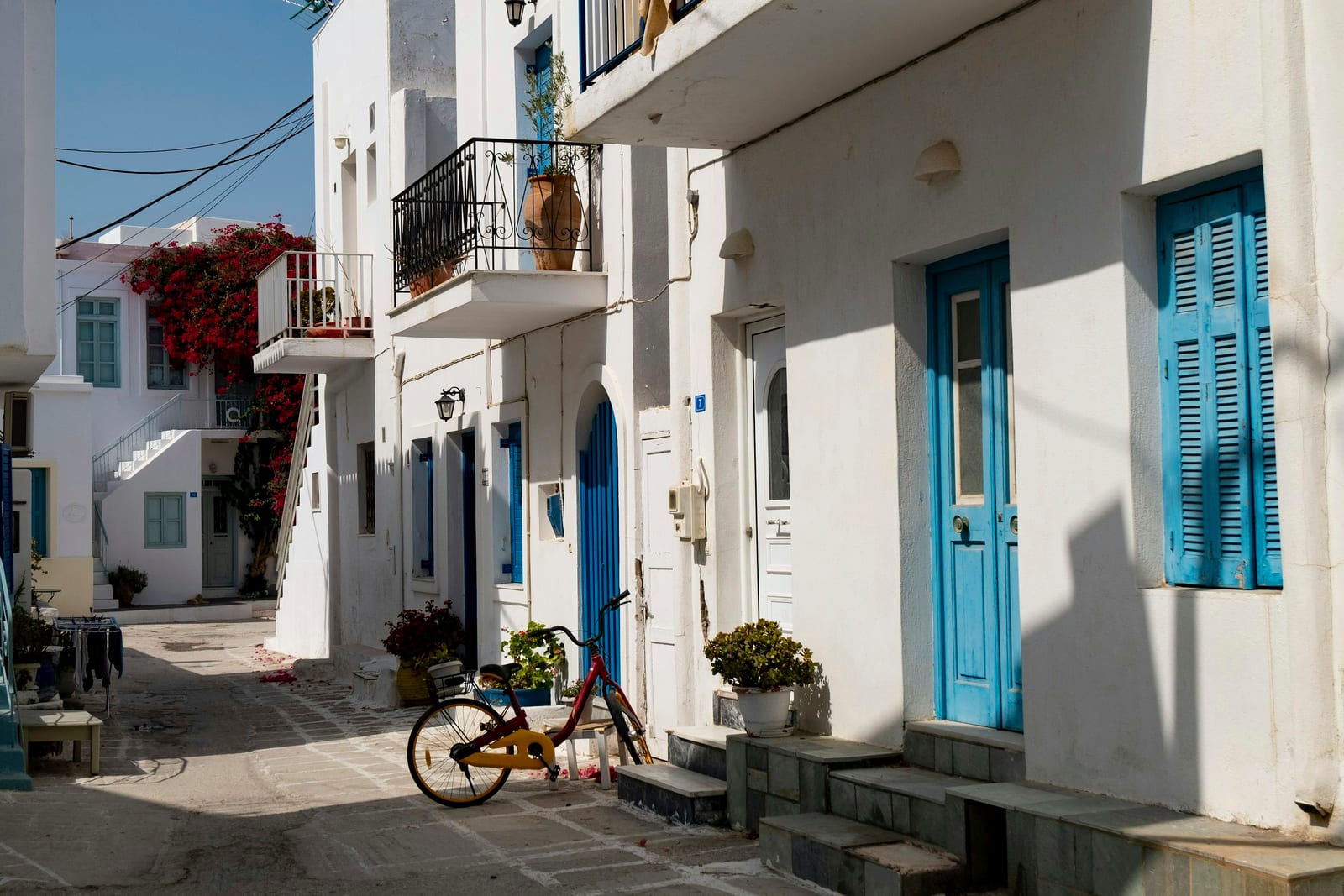 A bright white village street with blue doors, balconies, and a bicycle beside the steps.