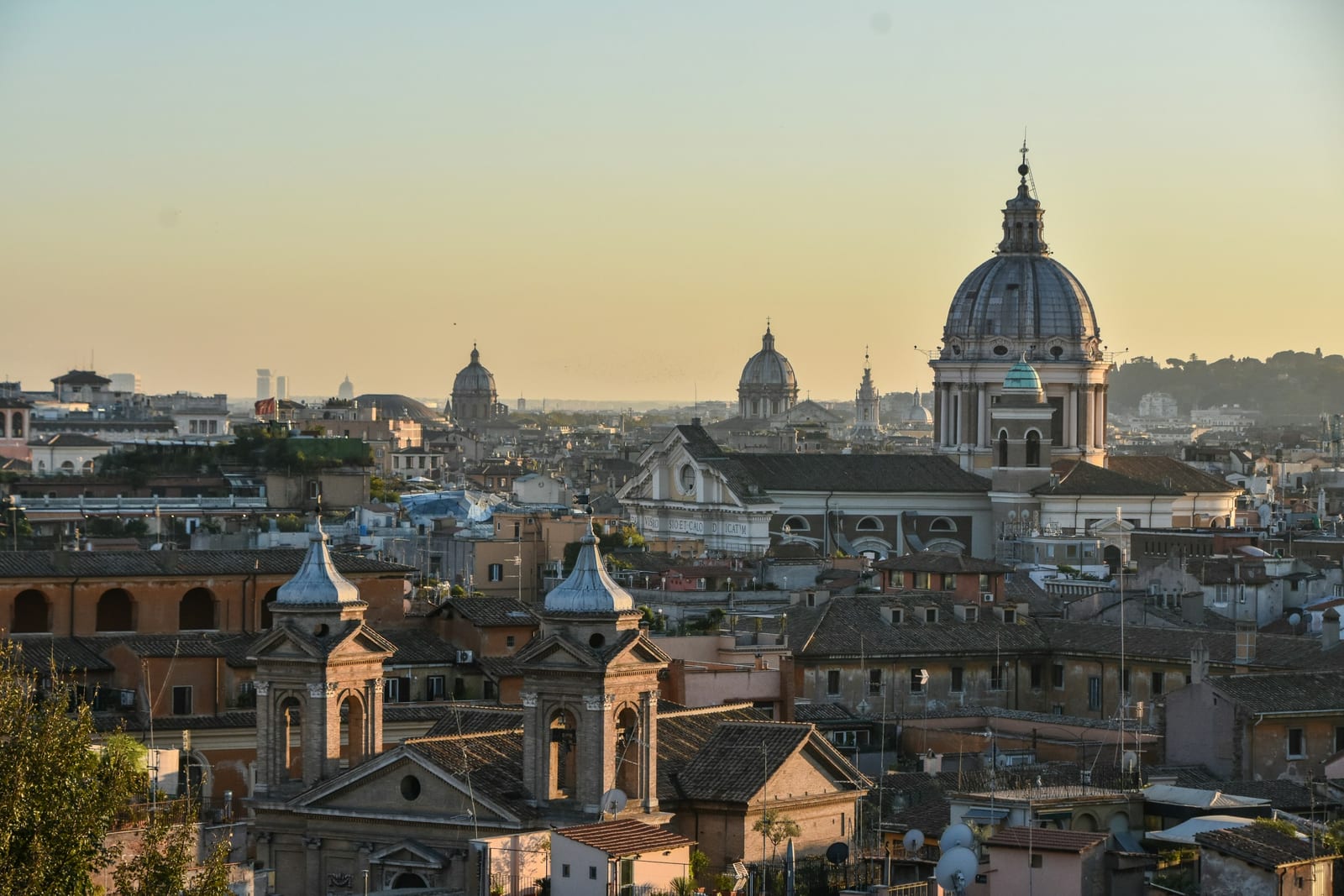 Rome's rooftops and church domes glowing under a golden sunset sky.
