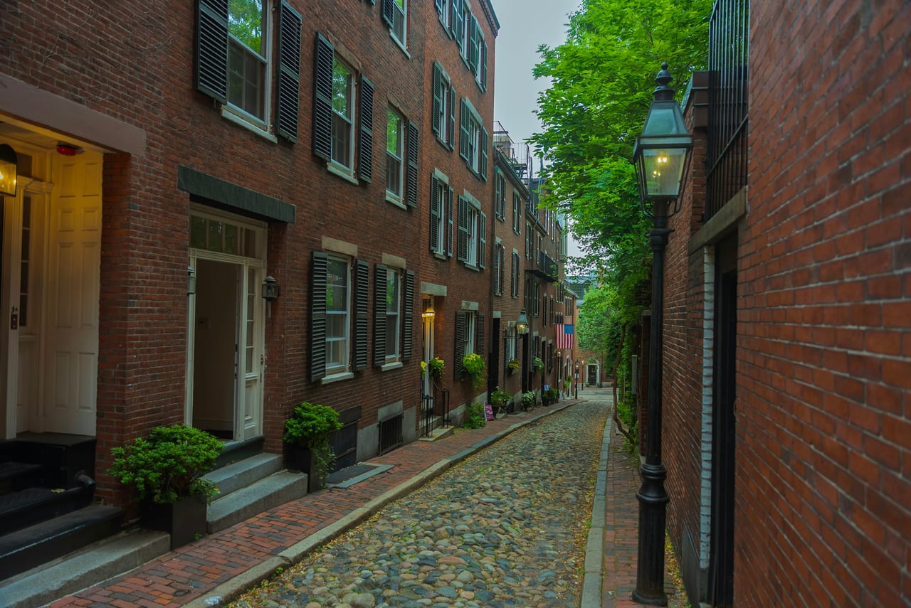 Red-brick rowhouses line Acorn Street in Beacon Hill, cobblestones and gas lamps catching the afternoon sun.