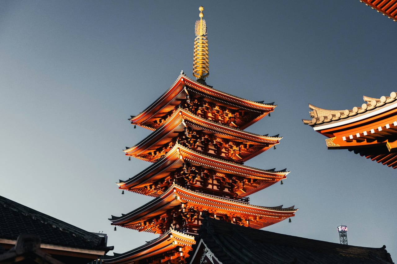 The five-story pagoda of Senso-ji stands against a clear blue sky beside the temple's carved eaves.