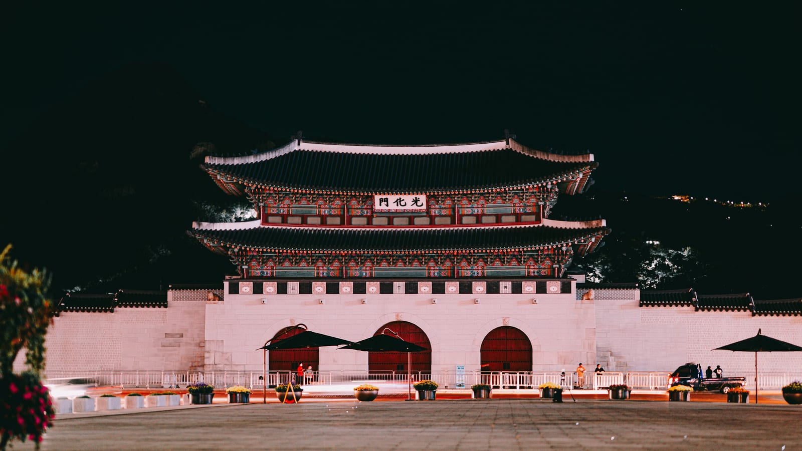 Gwanghwamun Gate is brightly lit at night, with its traditional palace roof and courtyard centered in the frame.