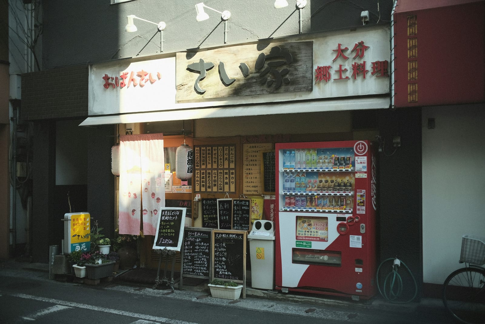 A small soba restaurant storefront with a menu board and a red vending machine.