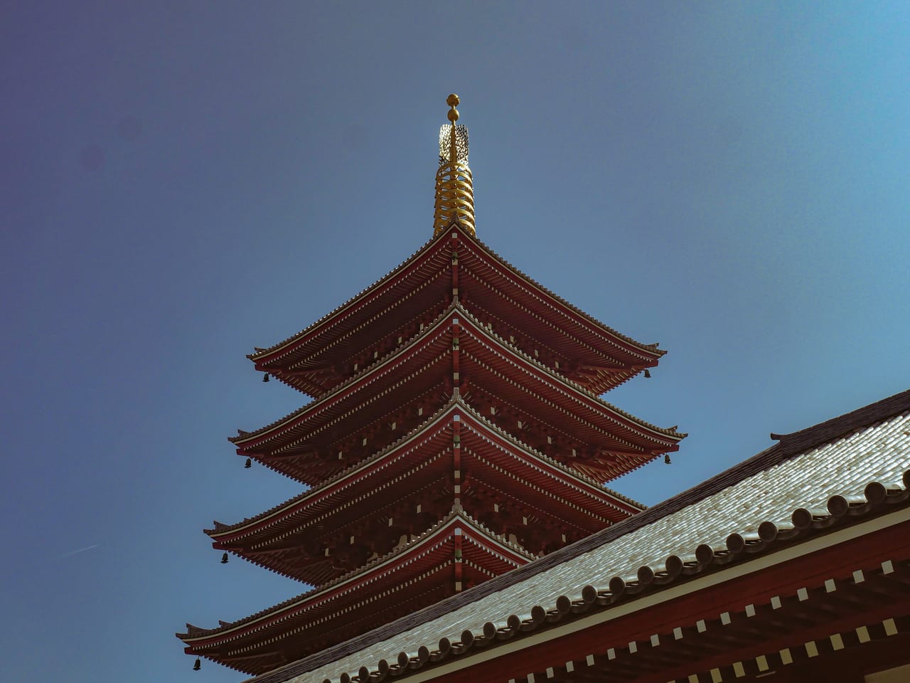 Senso-ji's vermilion five-story pagoda rises against a clear blue sky beside the temple's ornate eaves.
