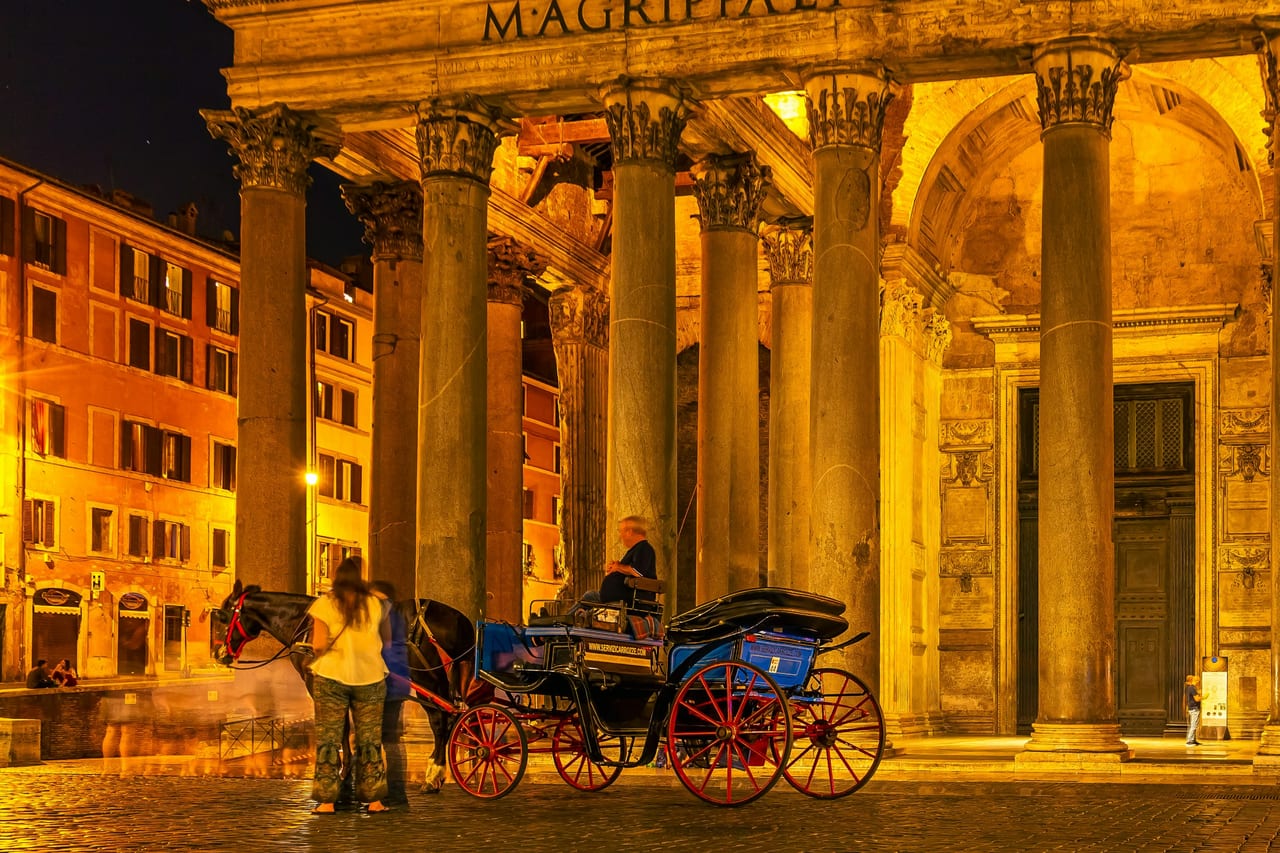 The Pantheon's granite columns and inscribed portico stand lit at dusk in Piazza della Rotonda.