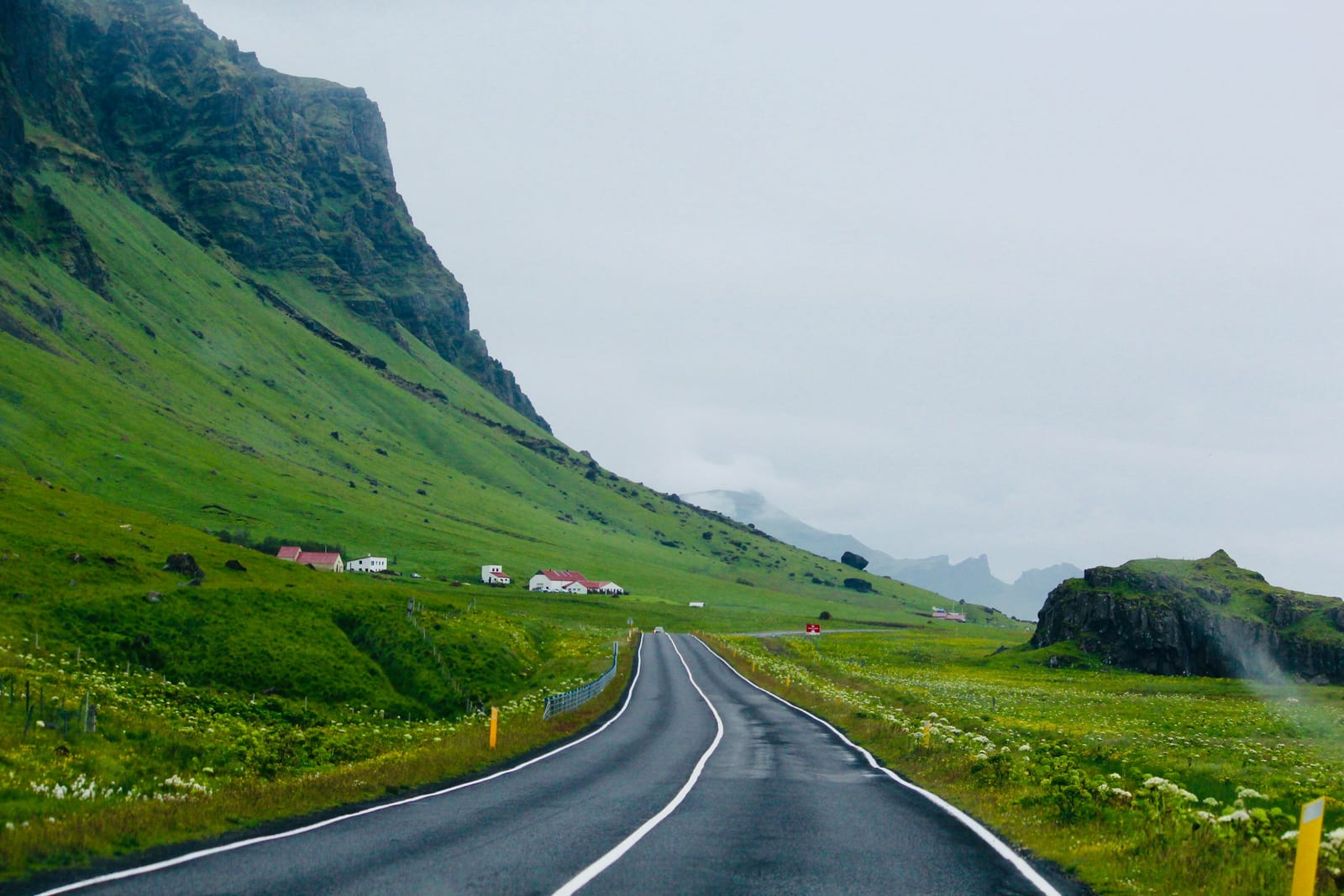 A paved road curves through a bright green Icelandic valley beneath steep mountains.