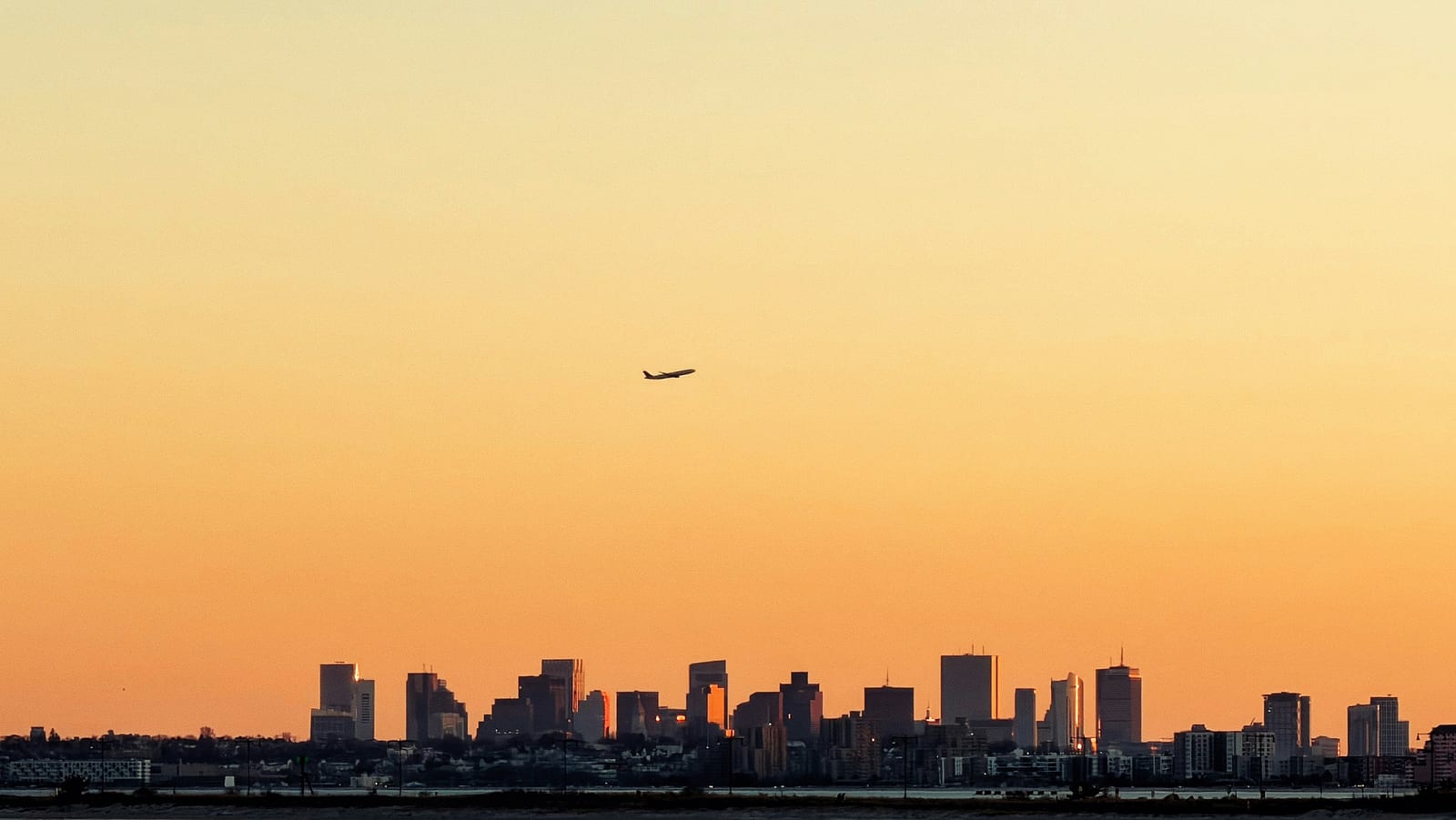 A passenger airliner descending toward a city at dusk.