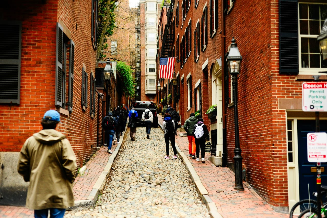 Cobblestoned Acorn Street in Beacon Hill lined with brick rowhouses, gaslamps, and autumn leaves.