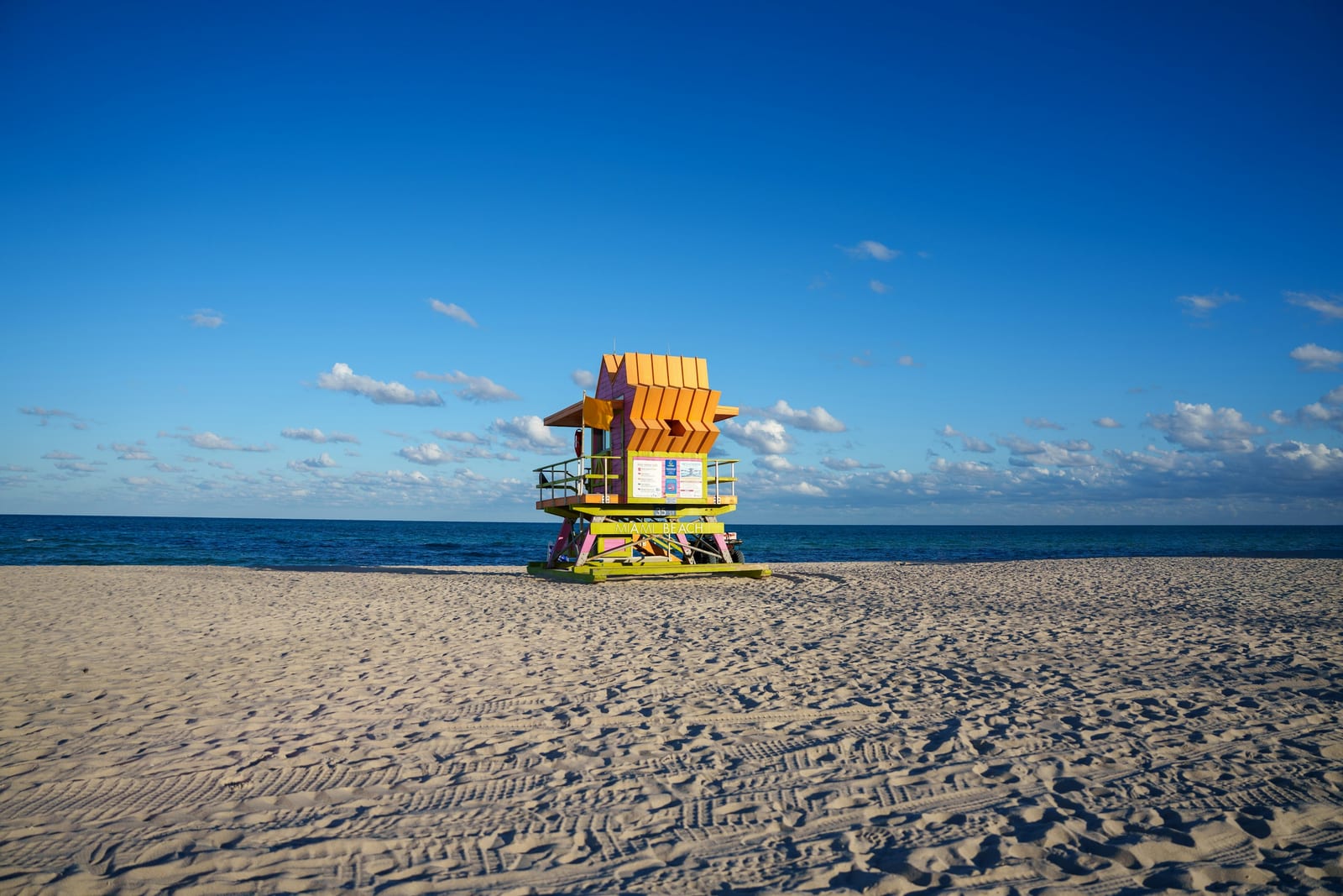 A brightly painted lifeguard tower stands on a sunny sandy beach beside the ocean.