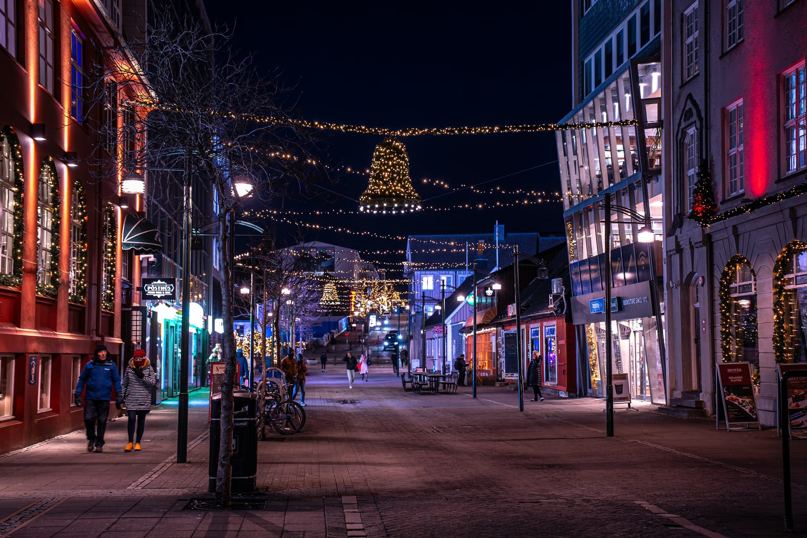 A brightly lit Reykjavik street lined with Christmas decorations and glowing shopfronts at night.