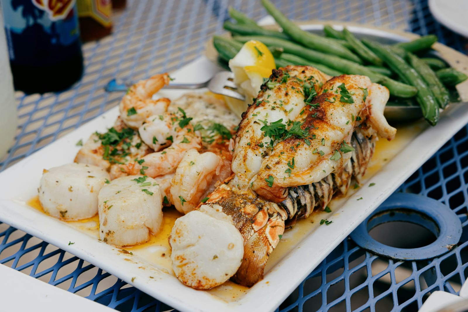 A plate of grilled fish, shrimp, scallops, and green beans sits on an outdoor restaurant table.