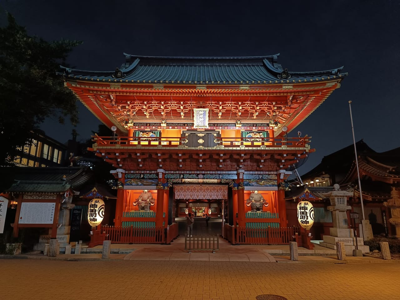 Kanda Myojin's ornate vermilion gate glows under its lanterns at dusk, the shrine's name lit across the paper globes.