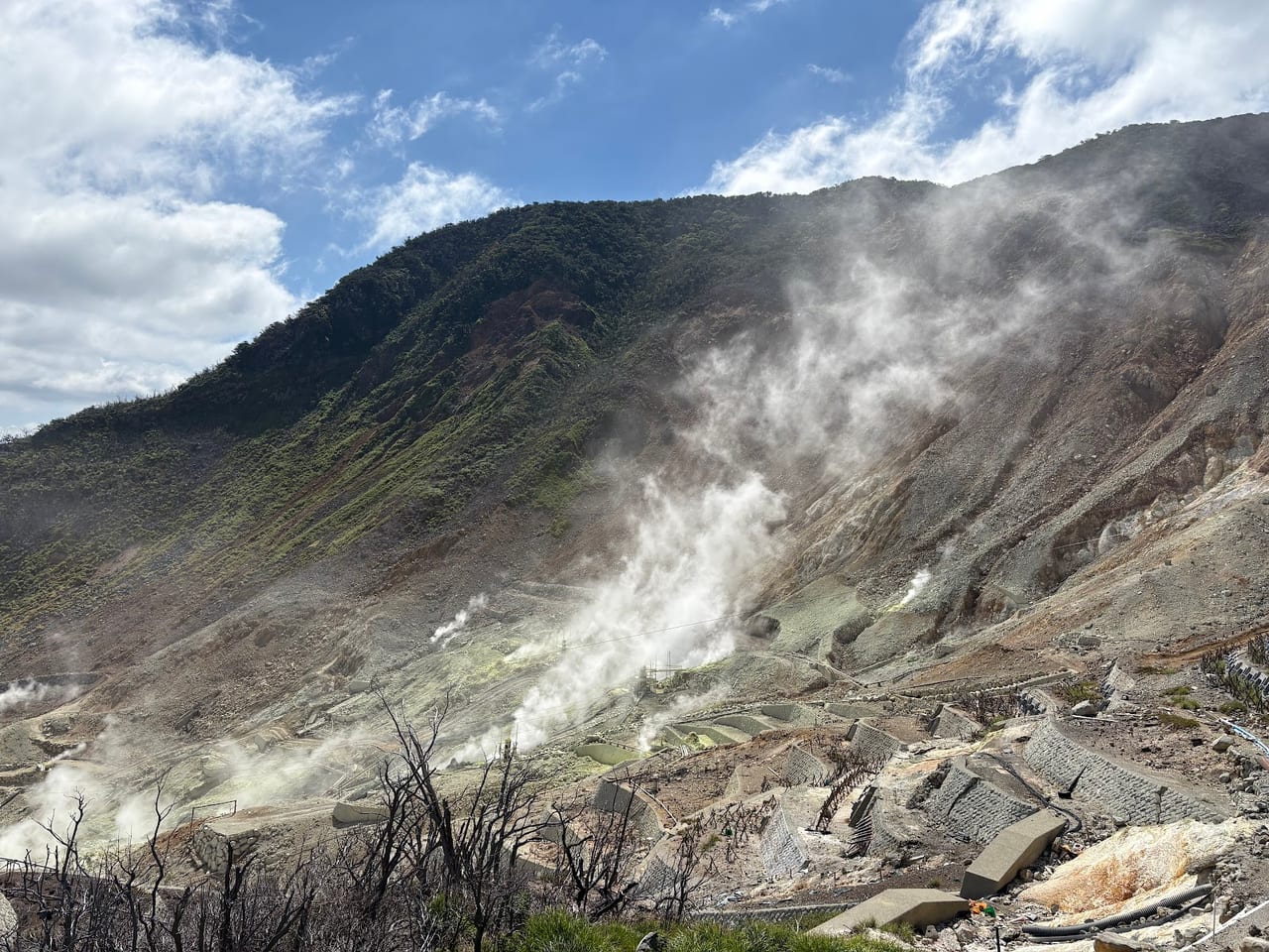 White sulphur steam rises from the barren slopes of the Owakudani volcanic valley under a blue sky.