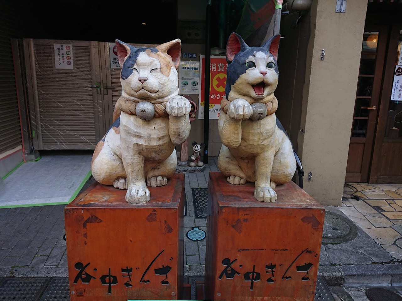 Two large painted wooden cats sit on stands lettered Yanaka Ginza at the entrance to the retro shopping street.