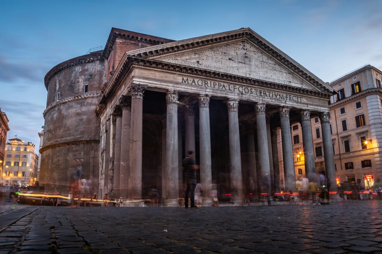 The Pantheon's granite columns and inscribed portico stand lit at dusk in Piazza della Rotonda.