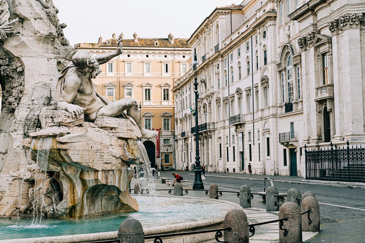 A river-god figure of Bernini's Fountain of the Four Rivers leans out over the water, the palazzi of Piazza Navona behind.