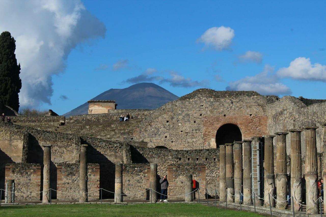 The colonnade and brick arch of Pompeii with Mount Vesuvius rising behind it.