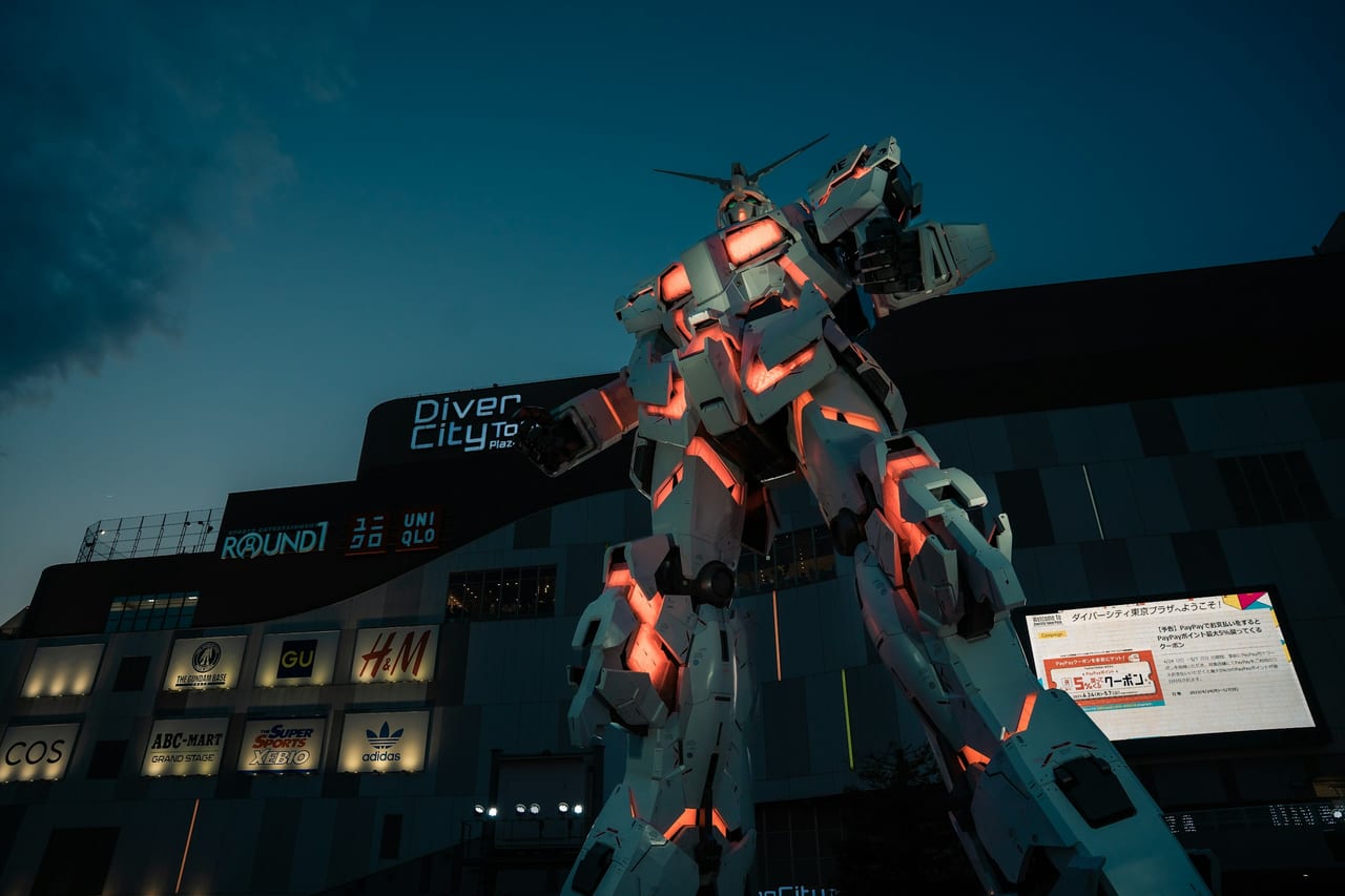 The life-size Unicorn Gundam stands lit in red outside the DiverCity mall on Odaiba after dark.