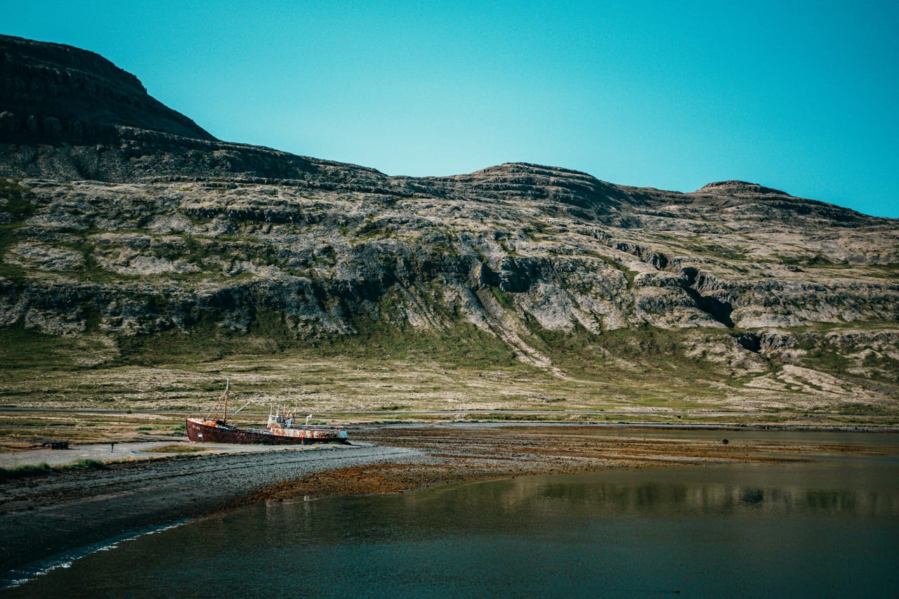 A rocky mountain rises above a calm body of water with a small boat near the shore.