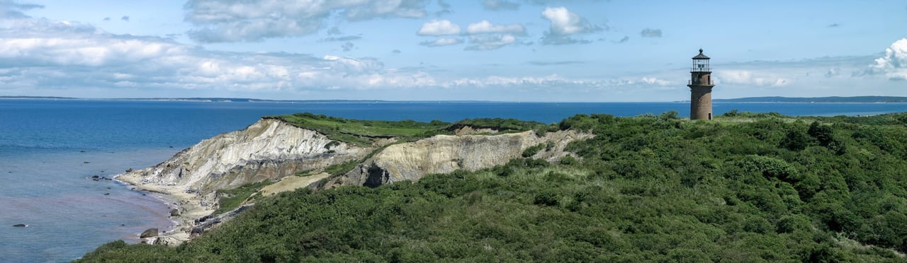 A lighthouse stands above white coastal cliffs and green vegetation beside the ocean.