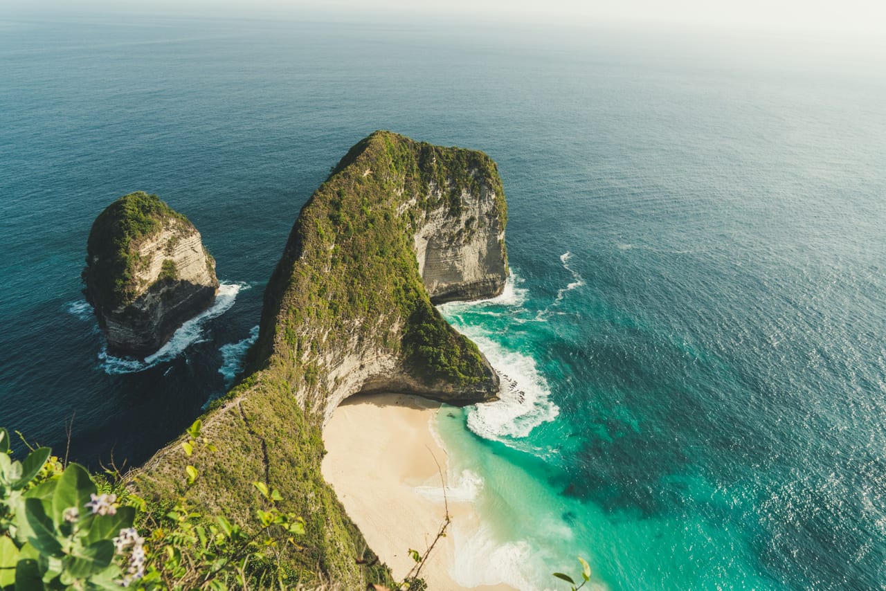 Aerial view of a green limestone headland, small offshore rocks, and a sheltered beach.