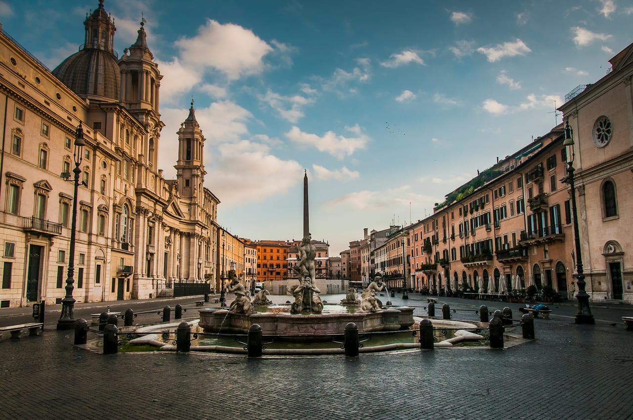 Piazza Navona opens out under a blue sky, its central obelisk and Bernini fountain framed by the dome and bell towers of Sant'Agnese.