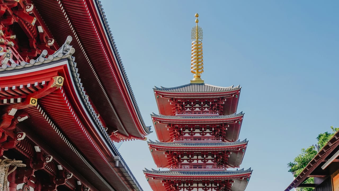 The five-story pagoda of Senso-ji stands against a clear blue sky beside the temple's carved eaves.